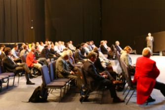 A group of exhibitors at a conference listening to a keynote speaker